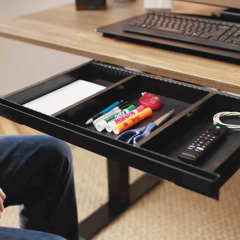 Black desk drawer with office supplies on a wooden desk